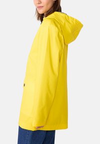 Veste imperméable jaune avec capuche, dotée d'une poche frontale et de détails en boutons, fabriquée à partir d'un matériau lisse et texturé.