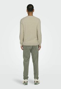Lichtbeige langemouwen shirt, grijze corduroy broek en atletiekschoenen met groene accenten. Eenvoudig ontwerp, zachte textuur en casual pasvorm.