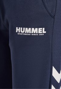 Navy urheiluhousut, joissa on valkoinen "HUMMEL" -logo ja "SPORTSWEAR SINCE 1923". Sivussa on viivamallinen chevron-kuvio.