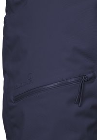 Marinblå vattentät jacka med en strukturerad yta, ficka med dragkedja och präglad logotyp för hållbarhet och funktionalitet.