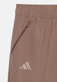 Καφέ παντελόνι με ελαστική μέση, τσέπη με φερμουάρ και ανακλαστικό λογότυπο Adidas σ το αριστερό μηρό.