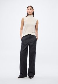 Bézs színű, ujjatlan garbó felső fekete, bőszárú nadrággal, finom textúrával és két oldalzsebbel. A fekete cipő egészíti ki a szettet.