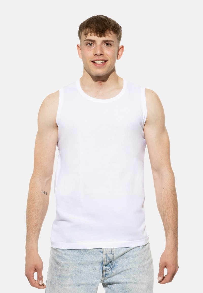 Débardeur blanc en coton, avec un col rond et sans manches. Porté avec un jean en denim bleu clair.