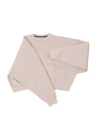 Przesadnie duża beżowa bluza wykonana z miękkiej bawełny, z długimi rękawami, okrągłym dekoltem, ściągaczami oraz małą metką marki przy dolnym brzegu.