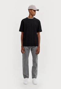 T-shirt noir à manches courtes texturé, pantalon droit gris, baskets blanches et casquette gris clair avec détails brodés.