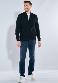 Black bomber jacket with a zip front, ribbed cuffs, and collar, paired with dark denim jeans and white sneakers. Plain background.