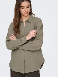 Olivgrünes, strukturiertes Hemd zum Knöpfen mit Kragen, langen Ärmeln und abgerundetem Saum. Hat eine lockere Passform und einen verdeckten Knopfverschluss.