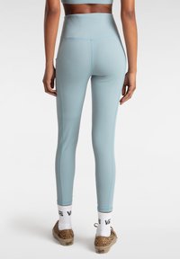 Leggings azzurri a vita alta con una texture liscia, cuciture a contrasto e una tasca laterale, abbinati a scarpe slip-on con stampa leopardata.