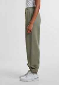 Olivengrønne, tapered sweatpants lavet af blødt stof, med elastisk talje og håndled, parret med hvide sneakers.
