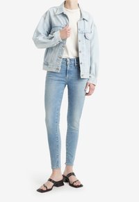 Ljusblå denimjacka med en avslappnad passform, bärs över en krämfärgad t-shirt och kombineras med slim fit ljusblå jeans och svarta klacksandaler.