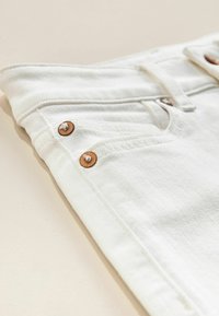 Weiße Denim-Jeans mit kupferfarbenen Knöpfen, Fünf-Taschen-Design und einer glatten Textur, mit einem gefalteten Bund für eine einfache Aufbewahrung.