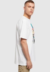 Hvid bomulds t-shirt med korte ærmer, der har et farverigt grafisk design på fronten. Lige snit med rund halsudskæring.