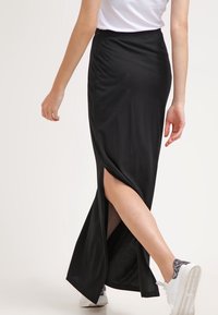 Musta maksihame joustavamateriaalista, jossa on sivuräystä ja liplatteva muotoilu. Yhdistetty valkoisiin lenkkareihin, esittäen rentoa ilmettä.