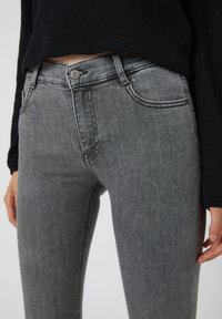 Jeans de mezclilla gris con corte slim, que presentan un diseño clásico de cinco bolsillos, cierre de botón y costura sutil en la cinturilla.