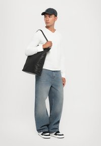 Sac en cuir noir avec une texture lisse, porté à l'épaule. Chemise légère à manches longues, jean en denim bleu ample et baskets noires et blanches.