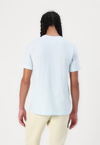 T-shirt en coton bleu clair avec des manches courtes, col rond et une texture simple et lisse, affichée de dos.