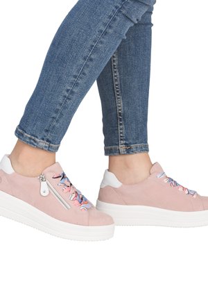 Person wearing light pink platform sneakers with colorful ribbon laces and zippers, paired with blue skinny jeans.