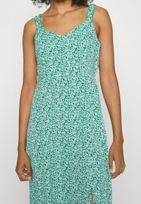 Vestido verde con estampado floral, con tirantes rizados ajustables, escote en V y una abertura lateral, hecho de una tela ligera con una textura suave.