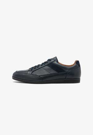 Sneaker di pelle blu navy a taglio basso con suola nera, chiusura con lacci e fodera interna color cammello su sfondo bianco.