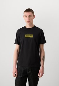Sorte bomulls-T-skjorte med et rektangulært logo i gult som leser "calvin klein" med "new york city" under, korte ermer og rund hals.