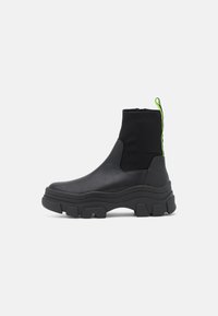 Svarta ankle boots med en kraftig sula, med en slät läder- och elastisk ovandel, samt en neongrön dragflik på baksidan.