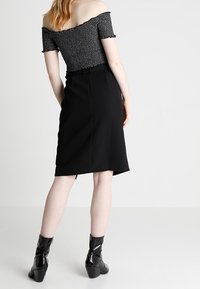 Czarna ołówkowa spódnica o gładkiej teksturze, połączona z dopasowaną, odkryta ramionami bluzką w czarno-białe wzory. Błyszczące czarne botki za kostkę.