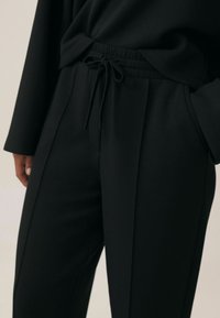 Czarne spodnie typu relaxed-fit wykonane z miękkiego materiału, z elastyczną talią i sznurkiem oraz bocznymi kieszeniami.