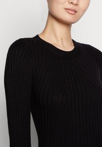 Maglione nero a coste con scollatura rotonda, caratterizzato da una texture verticale e maniche aderenti, realizzato in un morbido materiale knit.