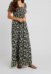 Maxiklänning i svart med blommönster, med fyrkantig halsringning, smockad byst, korta puffärmar och en flödande silhuett.