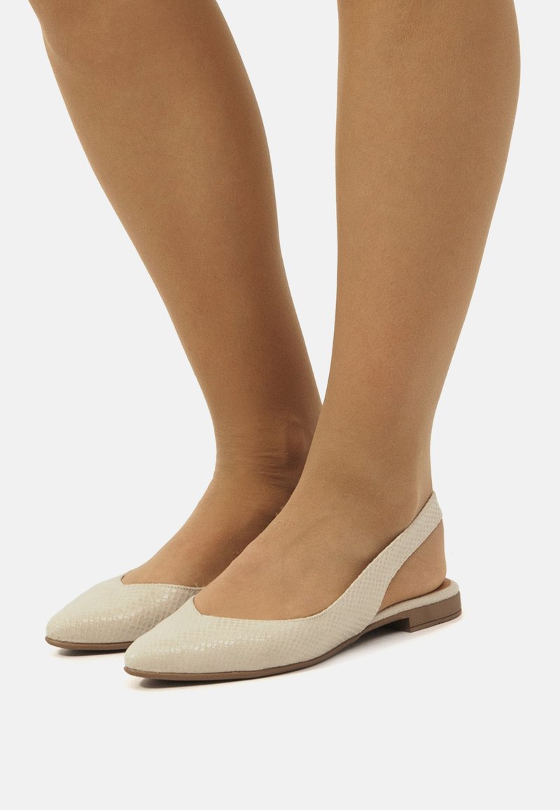 Ballerines beige à bride arrière avec une tige texturée, un bout pointu et un dos ouvert. Elles présentent une semelle plate et un design minimal sans quincaillerie visible.
