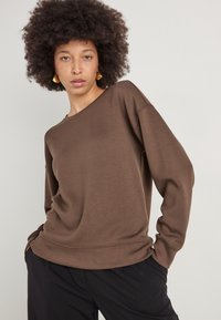 Brun, langærmet sweatshirt i blødt materiale med en afslappet pasform og rund halsudskæring, parret med sorte bukser.