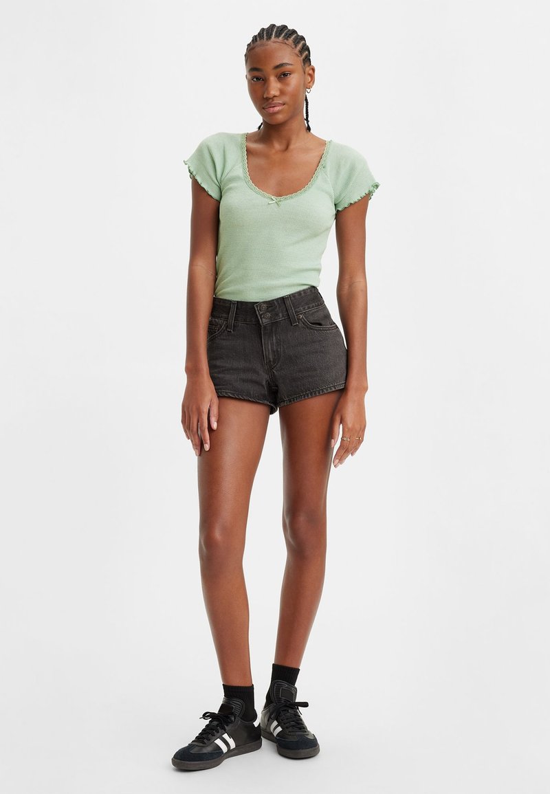 Top de manga corta acanalado en verde menta con escote cuadrado. Pantalones cortos de mezclilla negros de tiro alto. Zapatillas deportivas negras con detalles blancos.