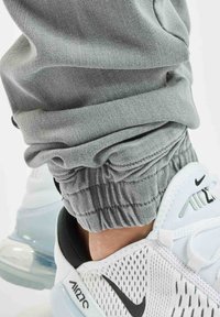 Ripresa ravvicinata di una persona che indossa joggers grigi chiari e sneakers Nike Air Max 270 bianche con il logo Nike visibile e suola con cuscinetto d'aria.