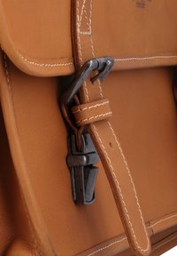 Tan leather bag with a flap closure, featuring a silver metal buckle and stitching details. Smooth texture with minimal wear.