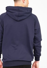 Marinblå huvtröja med ett mjukt, texturerat tyg. Har en justerbar huva och ribbade manschetter och nederkant. Enkel, enfärgad bakdesign.