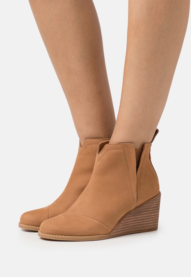 Bottines compensées couleur camel en daim souple avec un bout arrondi, des panneaux latéraux élastiques et un talon compensé texturé pour plus de stabilité.