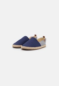 Marineblaue Leinensandalen mit beige gewobenen Jutesohlen, ausgestattet mit gestreiften Stoffakzenten und einem braunen Ledertab am Fersenbereich.