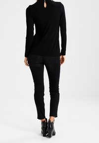 Svart långärmad topp med en nyckelhål bakom, tillsammans med svarta slim-fit jeans och ankelstövlar. Slätt tyg, figurnära design.