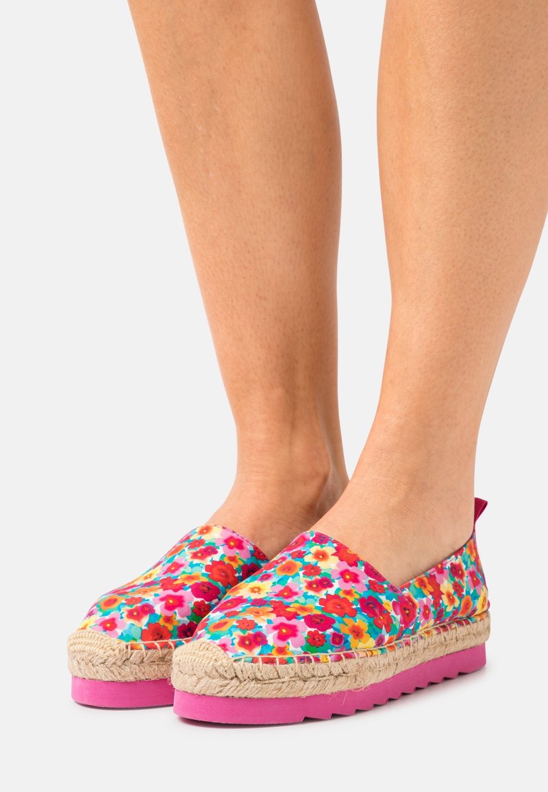 Espadrilles florales con parte superior de lona en colores vibrantes, suela de goma rosa y borde de yute trenzado. Diseño sin cierre con punta redondeada.