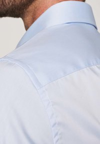 Camisa de color azul claro con un tacto suave y tejido. Primer plano de la costura en el hombro trasero y los detalles del cuello.