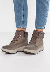 Grå ruskindsankelstøvler med en rund tå, tekstureret stofoverdel, dekorerede snørebånd og en sidelukning, sat på en chunky beige sål.