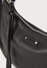 Borsa a tracolla in pelle nera con finitura texture, dotata di una cerniera argentata e di una toppa rettangolare con marchio, impreziosita da due borchie metalliche.