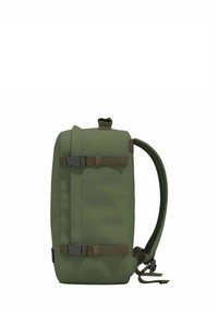 Vihreä kangaskäyttö-reppu, jossa on säädettävät hihnat, etuosan solkilukitus ja sileä pinta. Ominaisuuksiin kuuluu virtaviivainen suorakulmainen muoto.