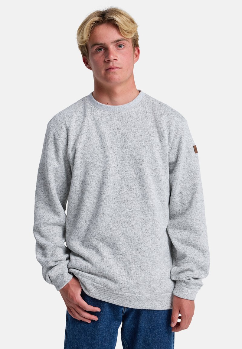 Sudadera de felpa gris claro con cuello redondo, puños y ribete inferior acanalados, y un pequeño parche de cuero marrón con el logo en la manga izquierda.