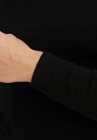 Pull en tricot noir avec des poignets côtelés. La texture est lisse avec un design ajusté, mettant en valeur un gros plan du bras et du poignet.