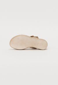 Beige suede sandal sole with textured surface and stitched edges, featuring a flattened heel and minimal detailing. Soft, flexible material.