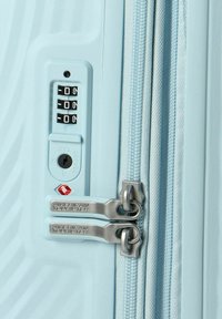 Valise rigide bleu clair avec verrou à combinaison, double fermeture éclair et fermetures métalliques. Présente une surface texturée pour une meilleure prise en main.