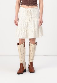 Bottes de cowboy marron avec un empeigne crème comportant des coutures décoratives. La partie inférieure est lisse, tandis que l'empeigne présente un design texturé.
