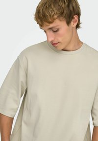 Lysebeige, oversized t-shirt lavet af blødt stof; har rund halsudskæring og korte ærmer, med en afslappet pasform og minimalistisk design.