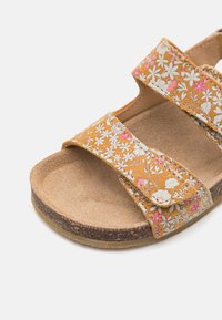Brune semskede sandal med blomster mønster remmer, med to justerbare Velcro-lukninger og en teksturert såle for grep.